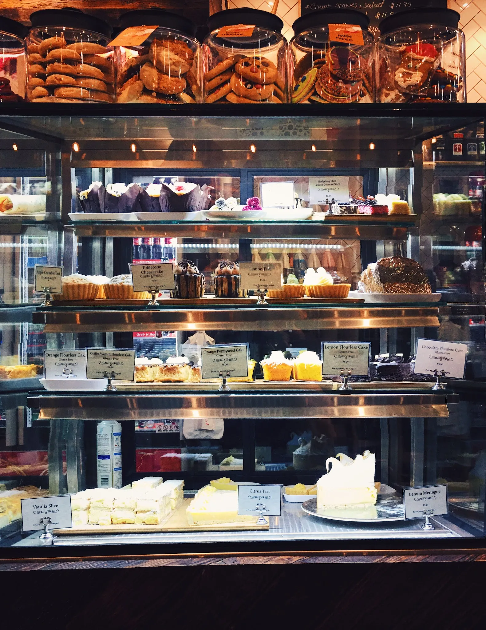 Four Seasons Café display cabinet stocked with cakes, slices, tarts and pastries on multiple shelves