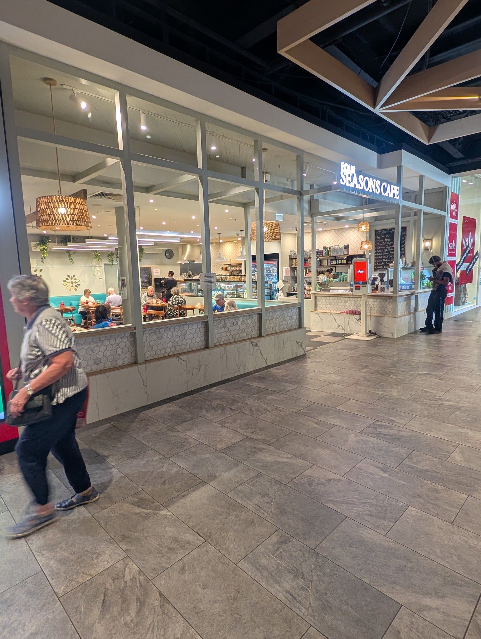 Wide exterior view of Four Seasons Cafe in shopping centre with glass frontage and a passing customer