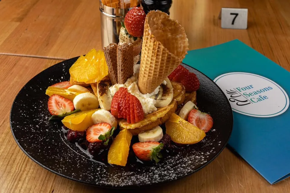 Loaded pancake stack with fresh fruit, waffle cones and cream next to a Four Seasons Cafe menu card