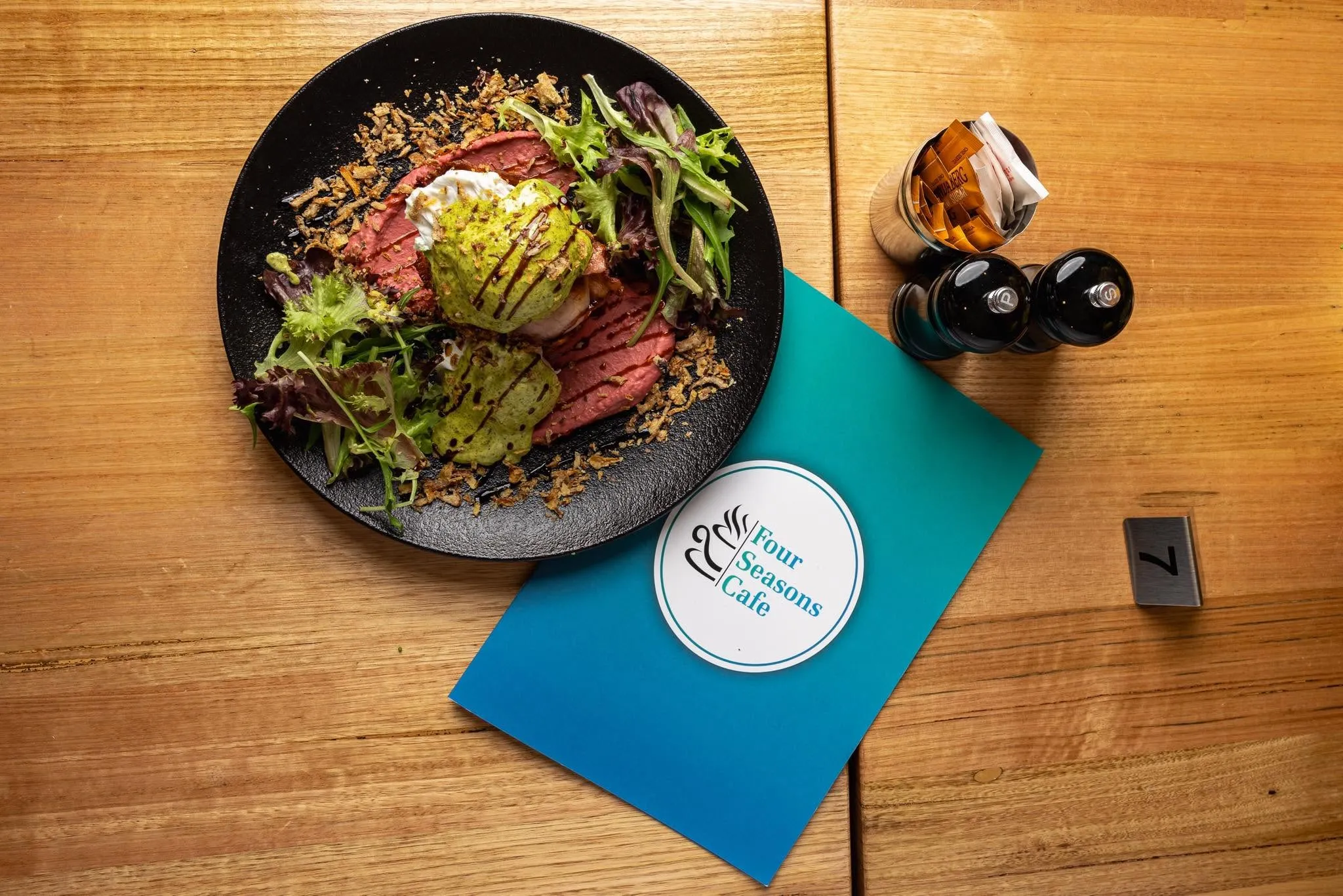 Overhead view of beef and egg breakfast dish on dark plate with Four Seasons Cafe branded menu card